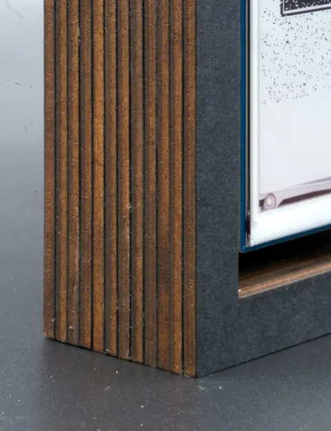A closeup of the left side of the object. The layers of brown cardboard with the thin slices of black paper between them, can be clearly seen.