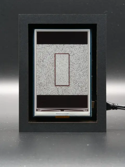 The object from the front. On its display there’s a light square with a clear dark outline, on a light grey background.