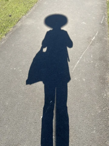 The shadow of a person with a remarkably circular, and remarkably large head. There’s a working clock in this circular head.
