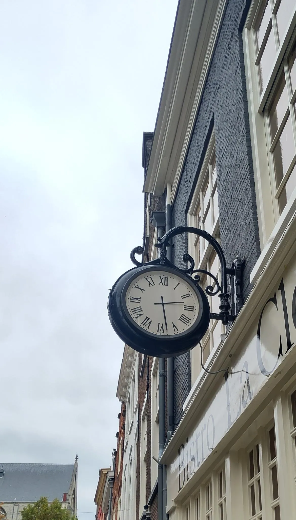 A classical clock attached to the facade of an old dutch house. It points at 28 minutes past two.