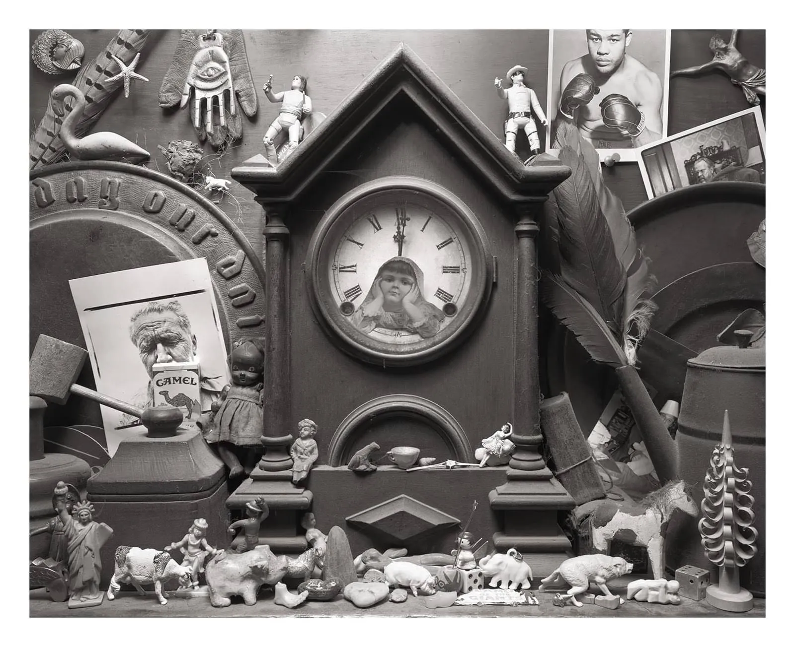 All kinds of toys, and pictures, and other stuff is placed around a wooden clock. On this clock a cutout picture of a girl is stuck. The clock points at one minute past 12.