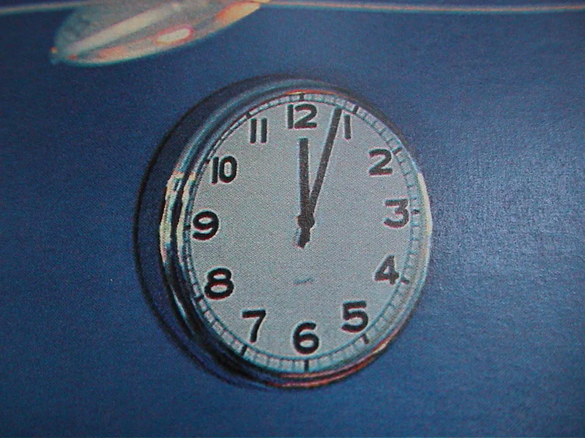 A clock on a blue wall says it is four minutes past twelve.