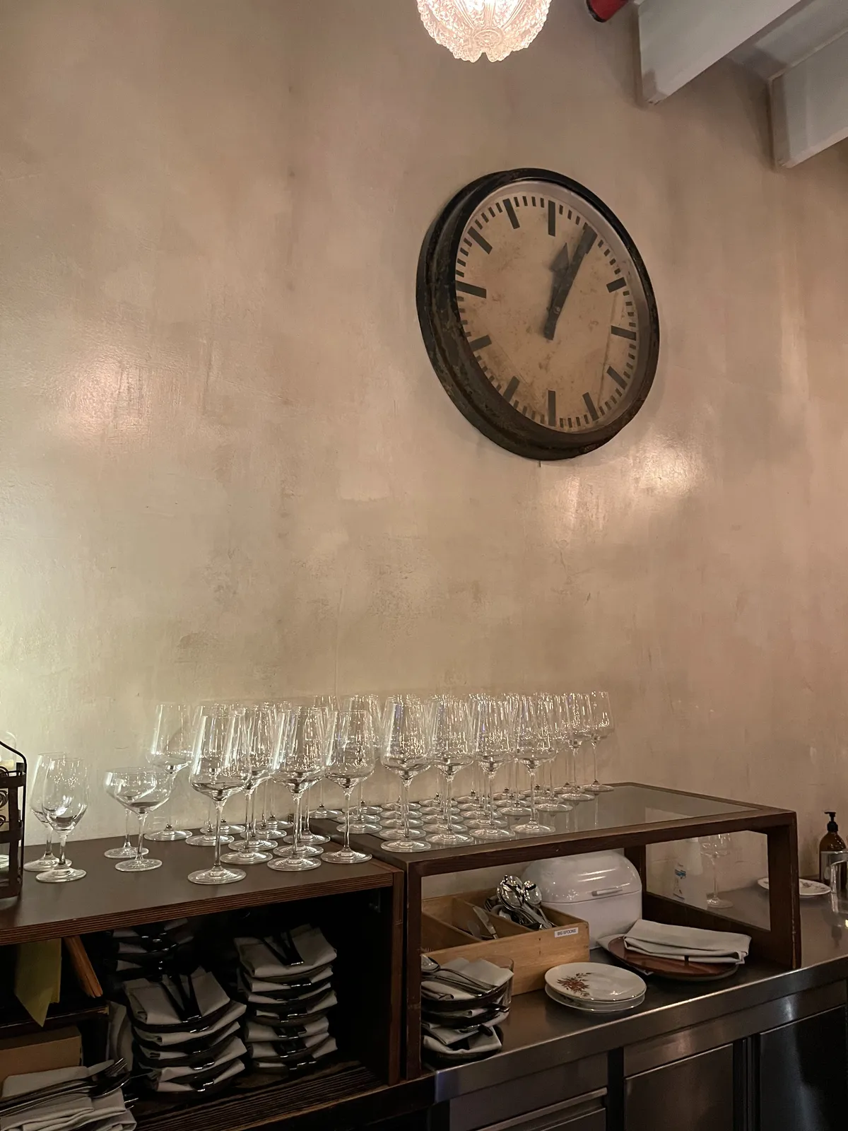Over a cabinet with clean linnen, and shiny wine glasses, there’s a large station clock, which points at 4 minutes past twelve.
