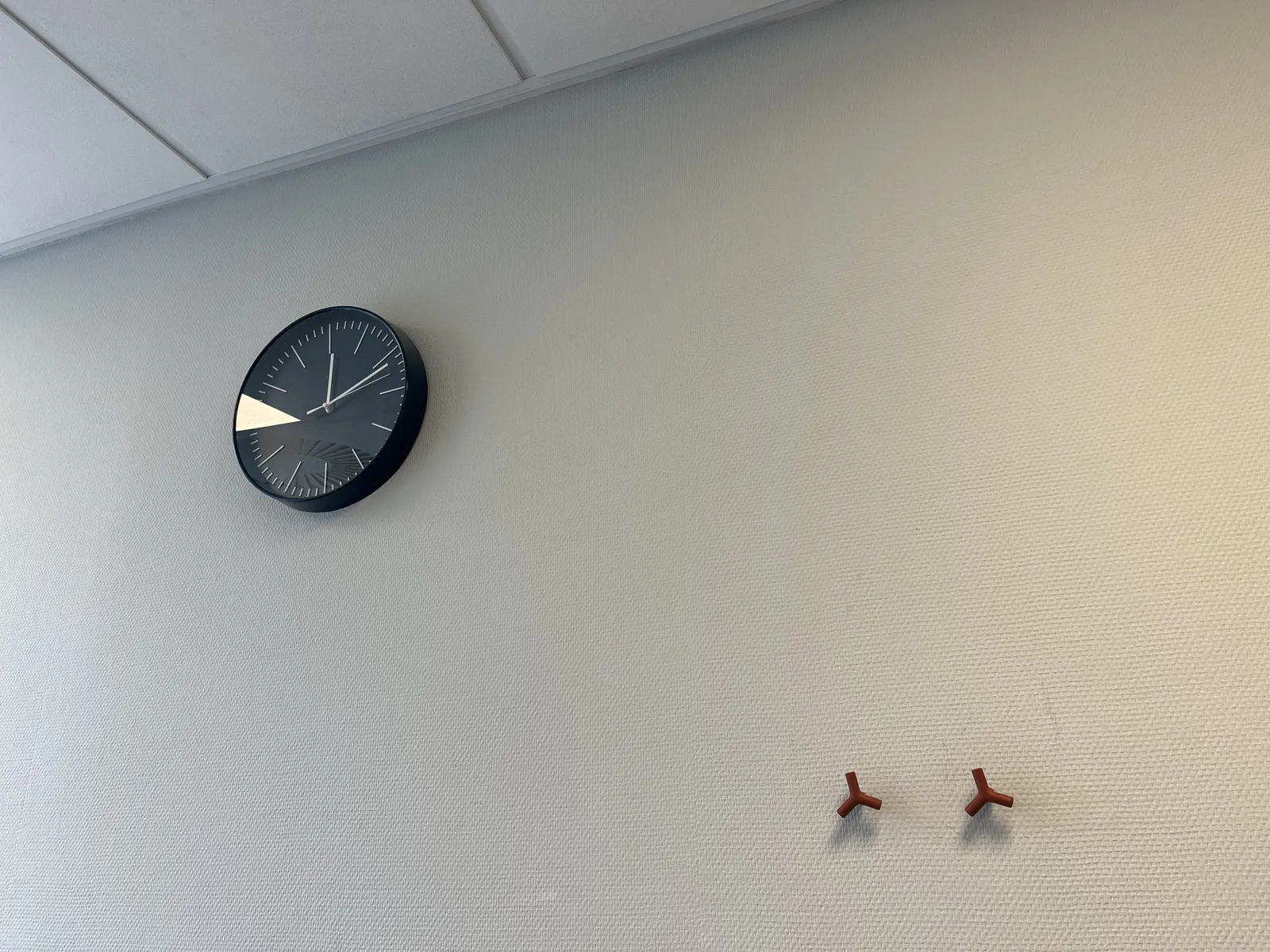 Two, red, three pointed stars on a white wall. There’s also a black and white clock on this same wall. It points at 11 minutes past twelve.