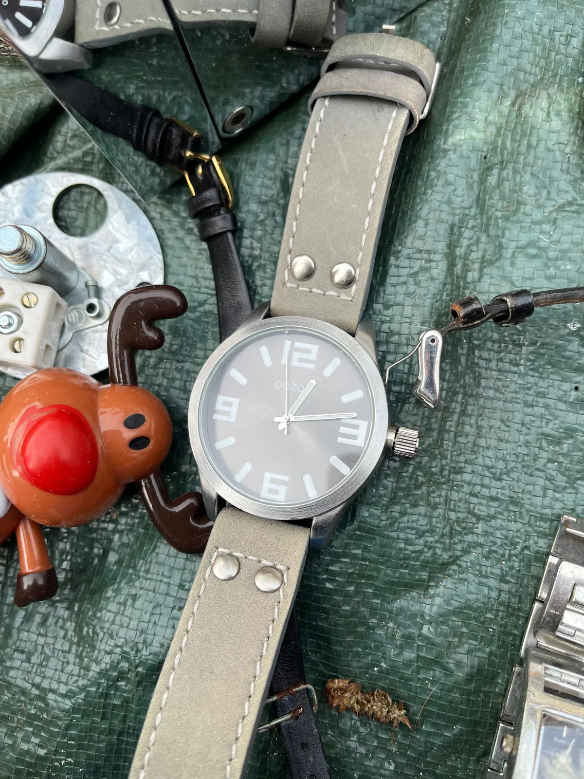 A watch surrounded by all kinds of stuff. It points at 12 past 12.