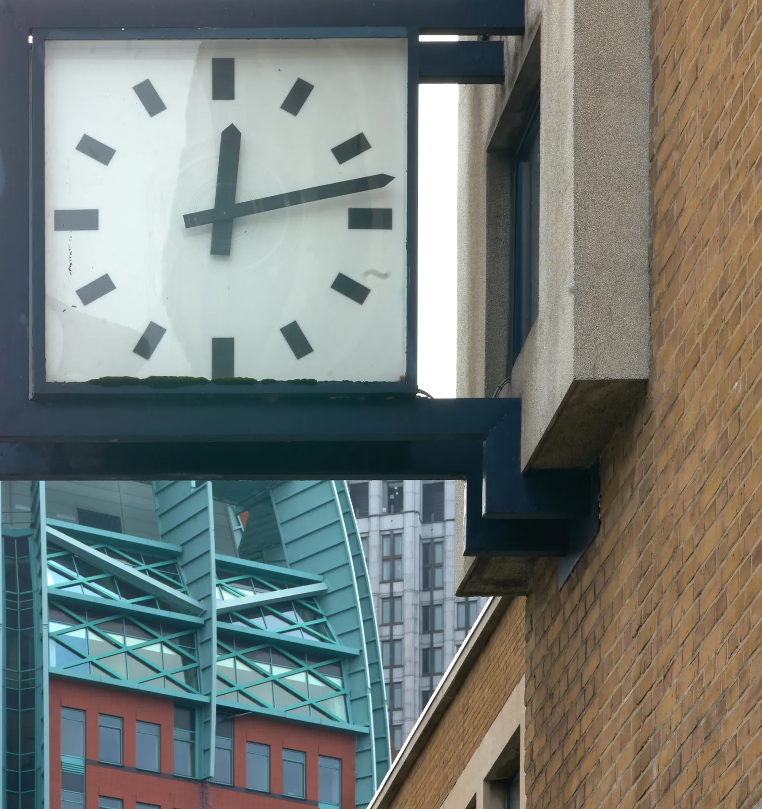 A modernist clock with a part of the Den Haag skyline in the background. The clock points at 13 past 12.