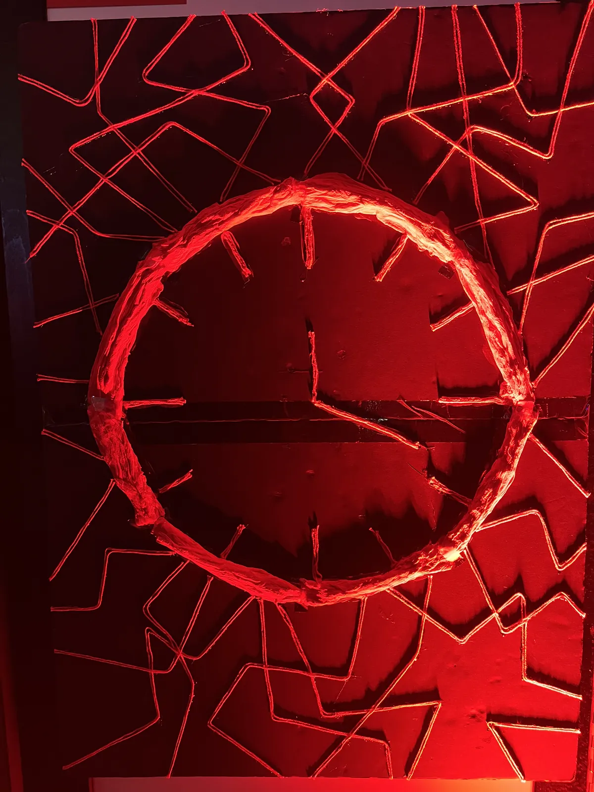 A clock made from some sort of woven fabric, lit with red light, points at 18 minutes past twelve.