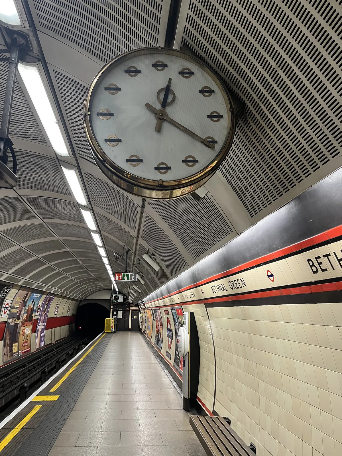 A clock on a platform in the subway in London, with the London Underground logo as hour indicators. The clock points at 20 past twelve.