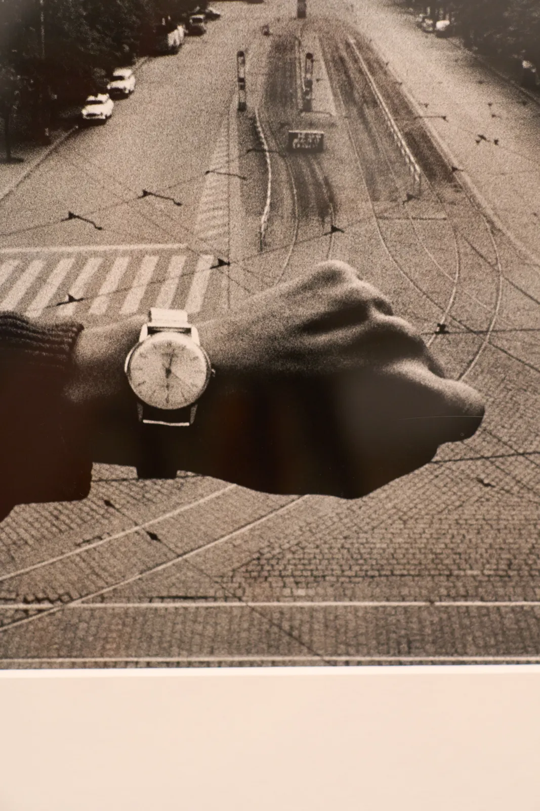 A picture taken from a framed black and white photograph. On this photograph there’s a cityscape and an arm which shows a watch. The watch points at 22 minutes past twelve. 
