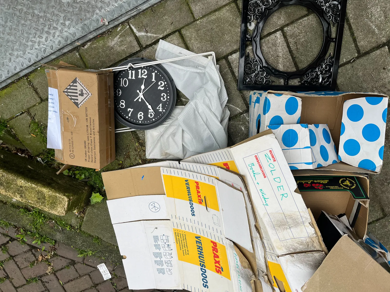 Among some rubbish on a street there’s a discarded clock. It points at 23 minutes past 12.
