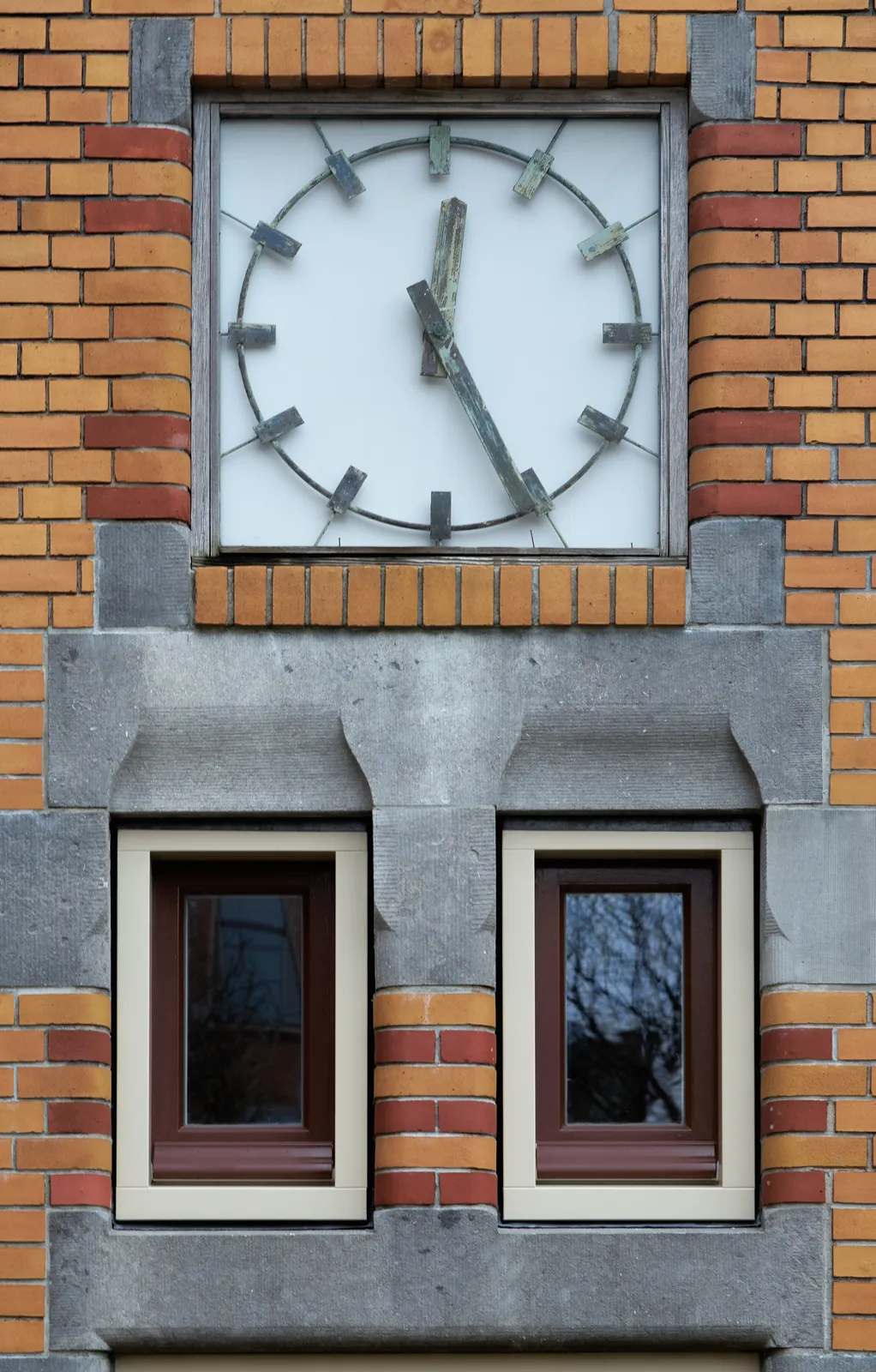 A square clock with some fine details, built into a wall in Amsterdam School style, points at 26 past 12.