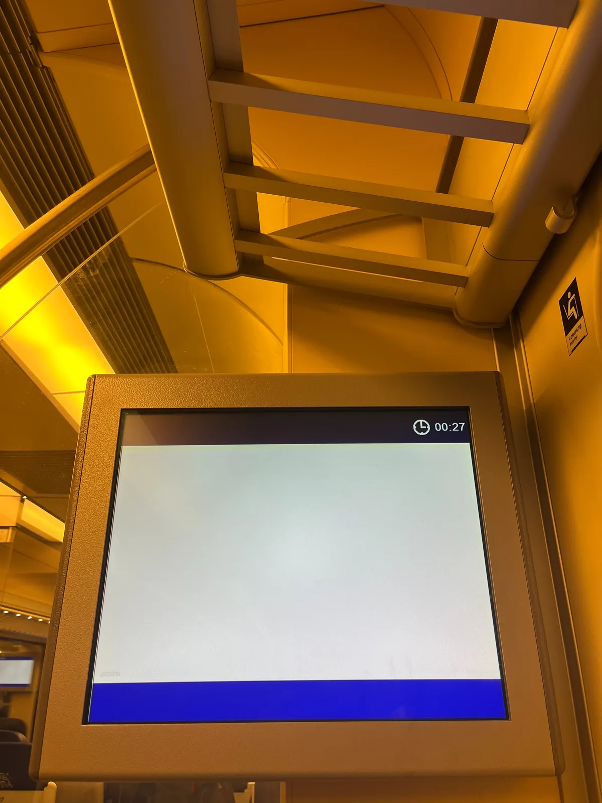 A luggage rack in a train with below it an empty information display. Well, not completely empty, it does show the time as 00:27.
