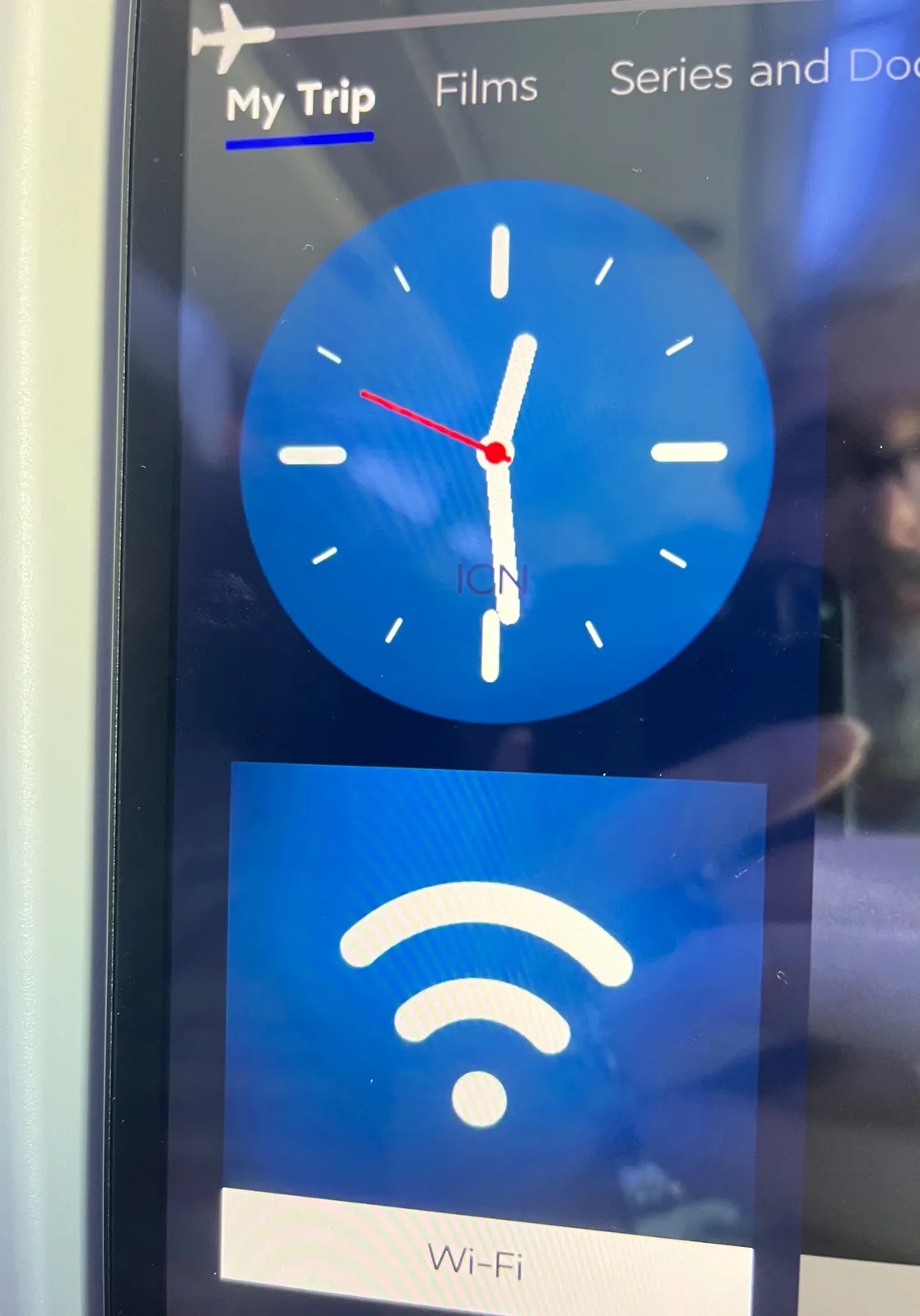 A clock on a display of what seems to be an in flight entertainment system, in an airplane. This clock points at 29 minutes past 12