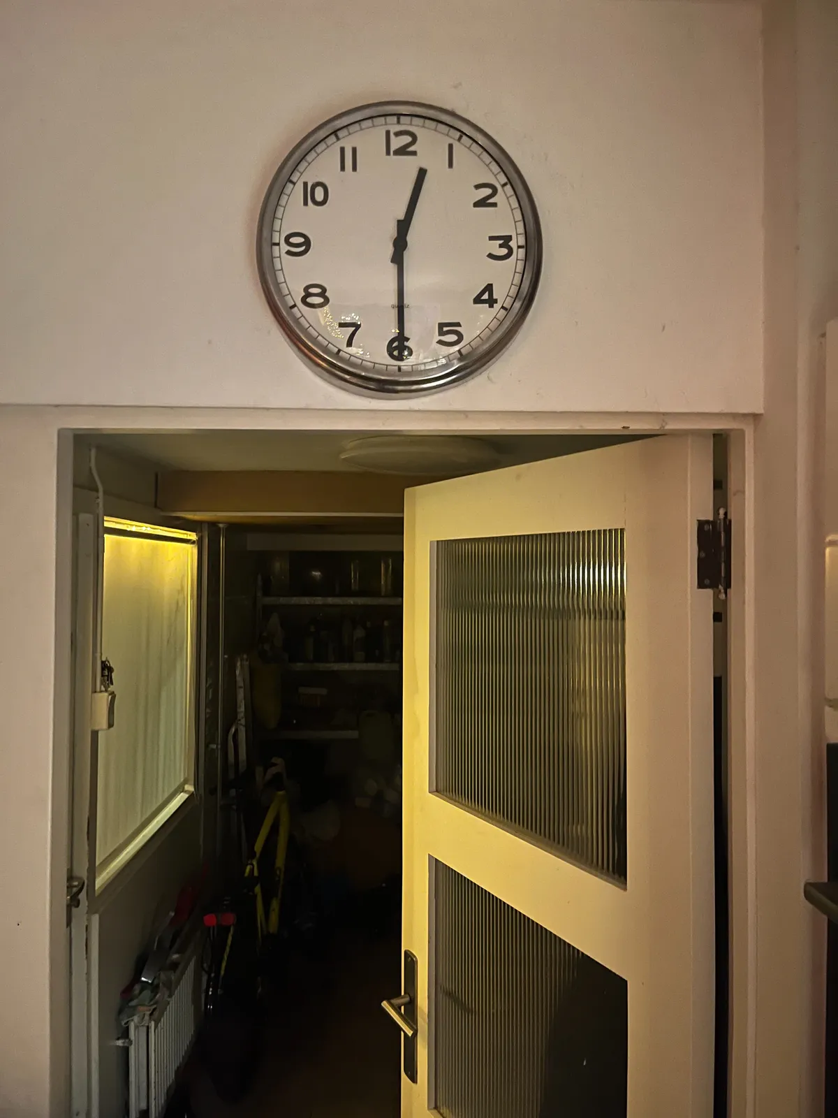 Looking through a door at a storage room. Above the door there’s a clock that points at half past twelve.