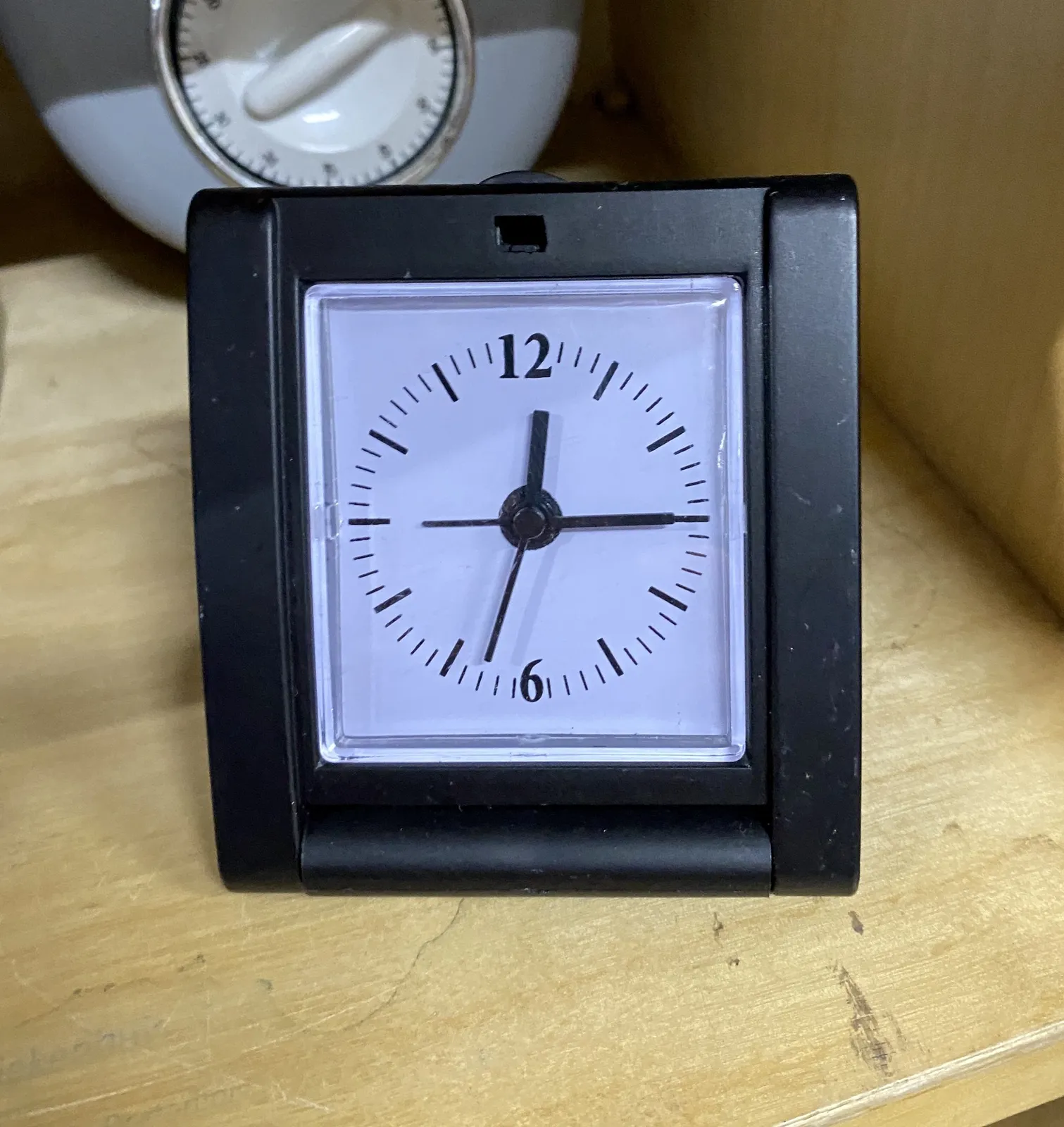 A little travel clock that points at 27 minutes to one.