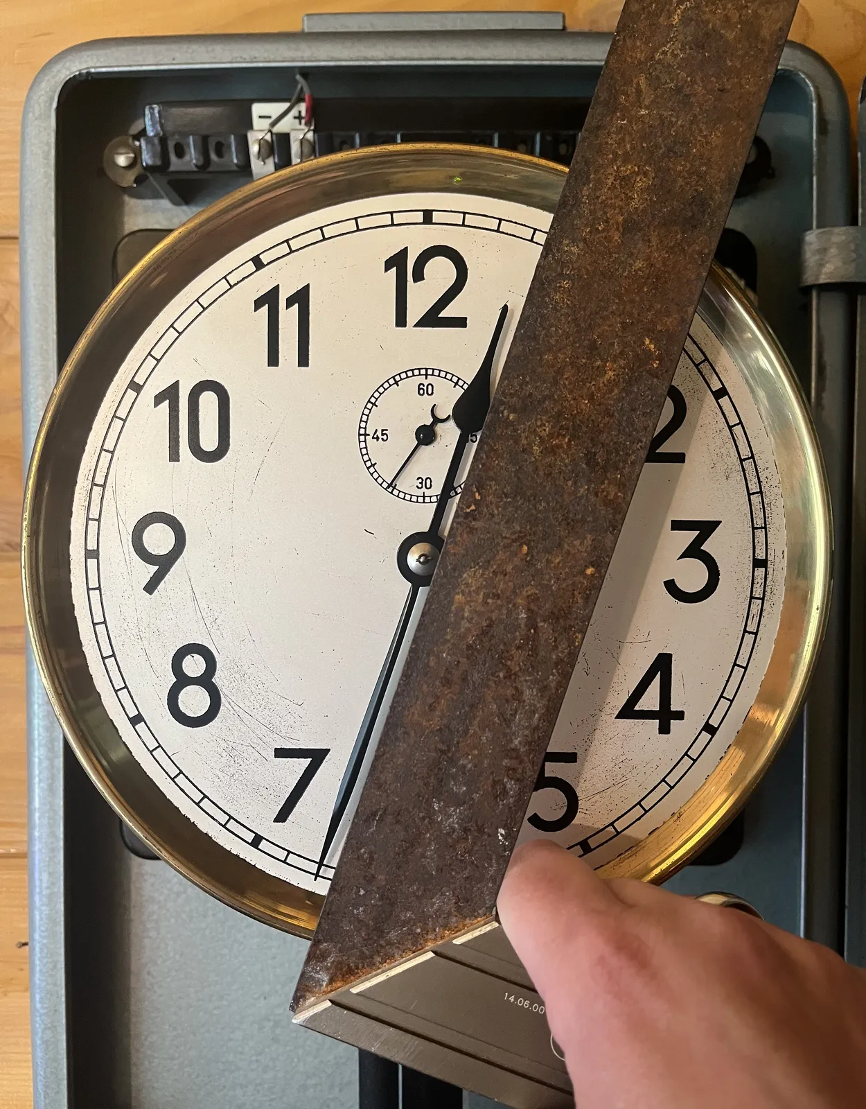 Someone is holding a try square in front of a clock, to show that the two hands of this clock form a perfect 180 degree angle at a 33 minutes past 12