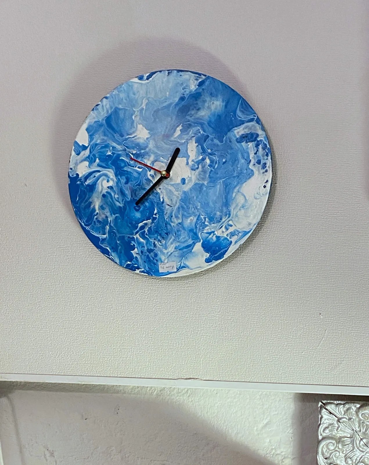 A blue and white clock, the decoration on its face looks a bit like clouds. Its face is rather large when you compare it to its hands. It seems to point at approximately 37 minutes past 12.