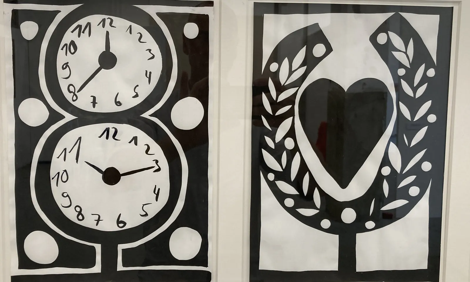 Two black and white art prints. The one on the right shows a heart and a laurel wreath. The one on the right shows two clocks. The one on top points at 40 minutes past 12, the one on the bottom at a quarter past 11.