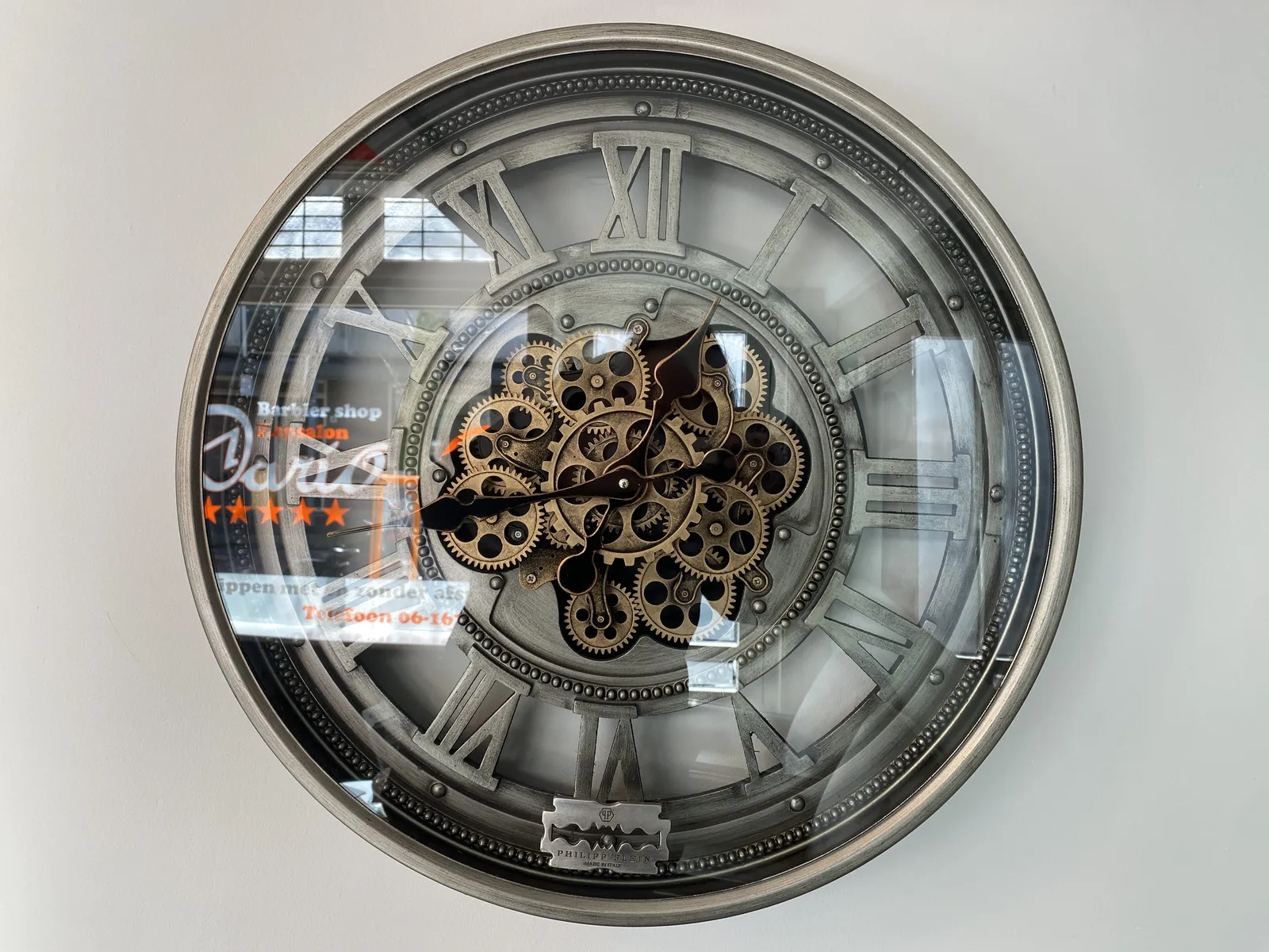A shiny transparent clock, with lots and lots of cogwheels in it, points at 42 past twelve.