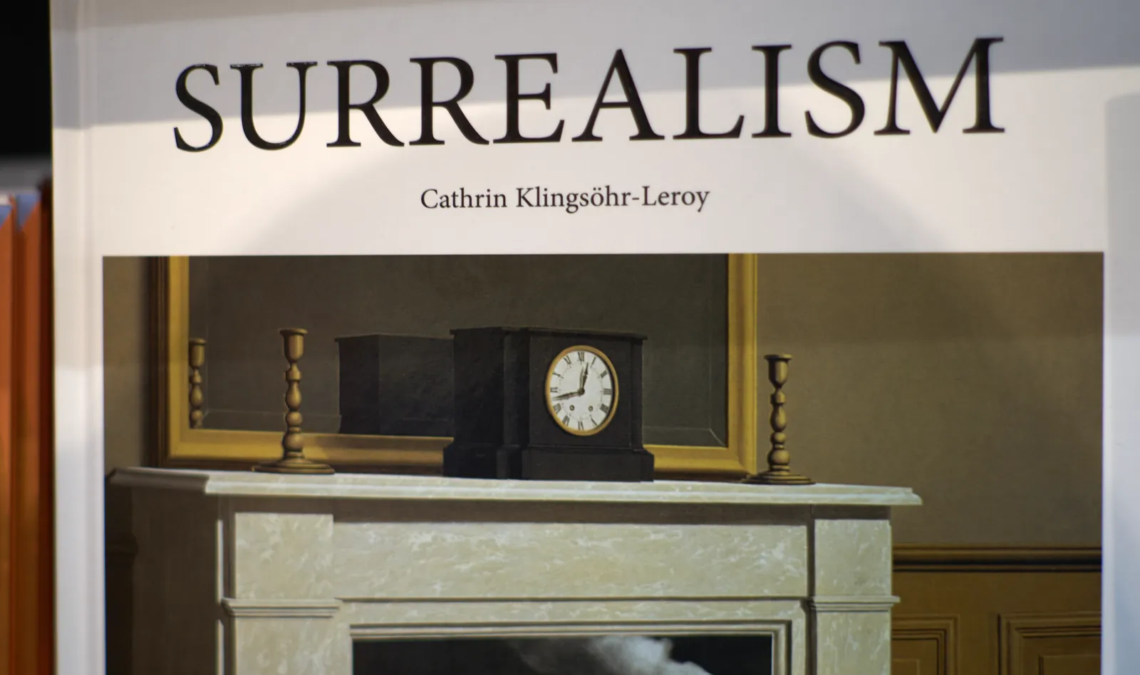 A picture taken from a book cover. The title is Surrealism, and it’s written by Cathrin Klingsöhr-Leroy. On this book cover is a reproduction of a painting. There’s a mantel clock on this painting which points at 18 minutes to one.