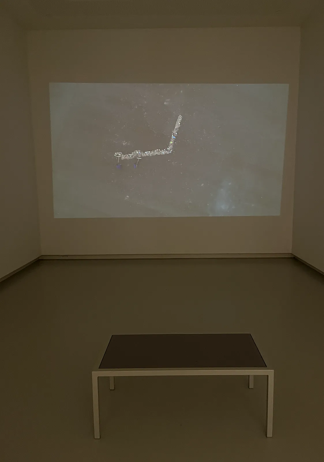 In a museum, looking at a clock that’s being projected on the wall. There‘s a bench to sit on, it’s empty. When you look closely you can see that the clock is in fact a movie, filmed from above. Two people are continuously sweeping leaves around a huge clock face. These sweeped leaves form the hands of the clock. At the moment the point at approximately 17 minutes to one. 