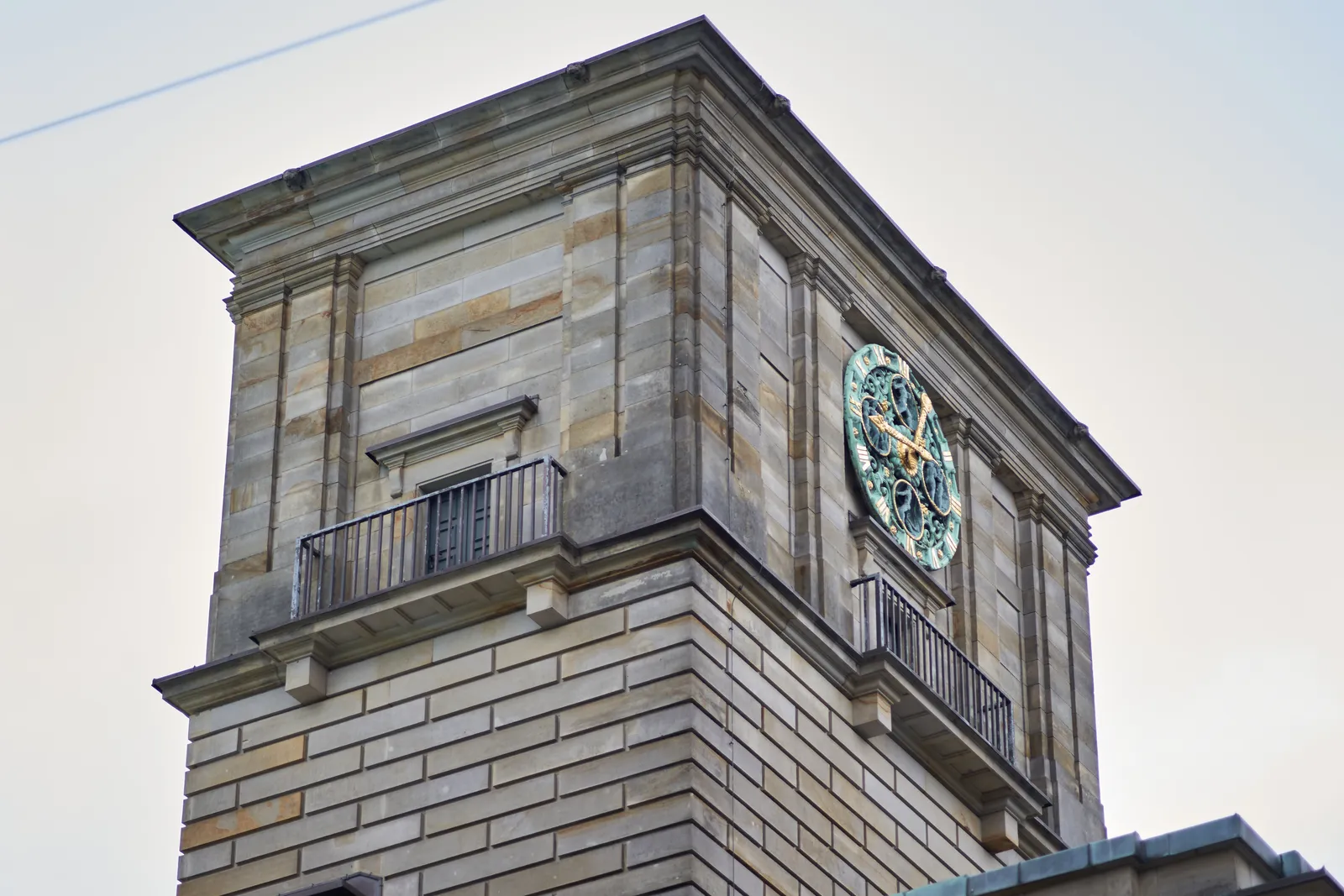 An ornamented clock with copper and gold on top of a high building. It points at approximately 16 minutes to 1.