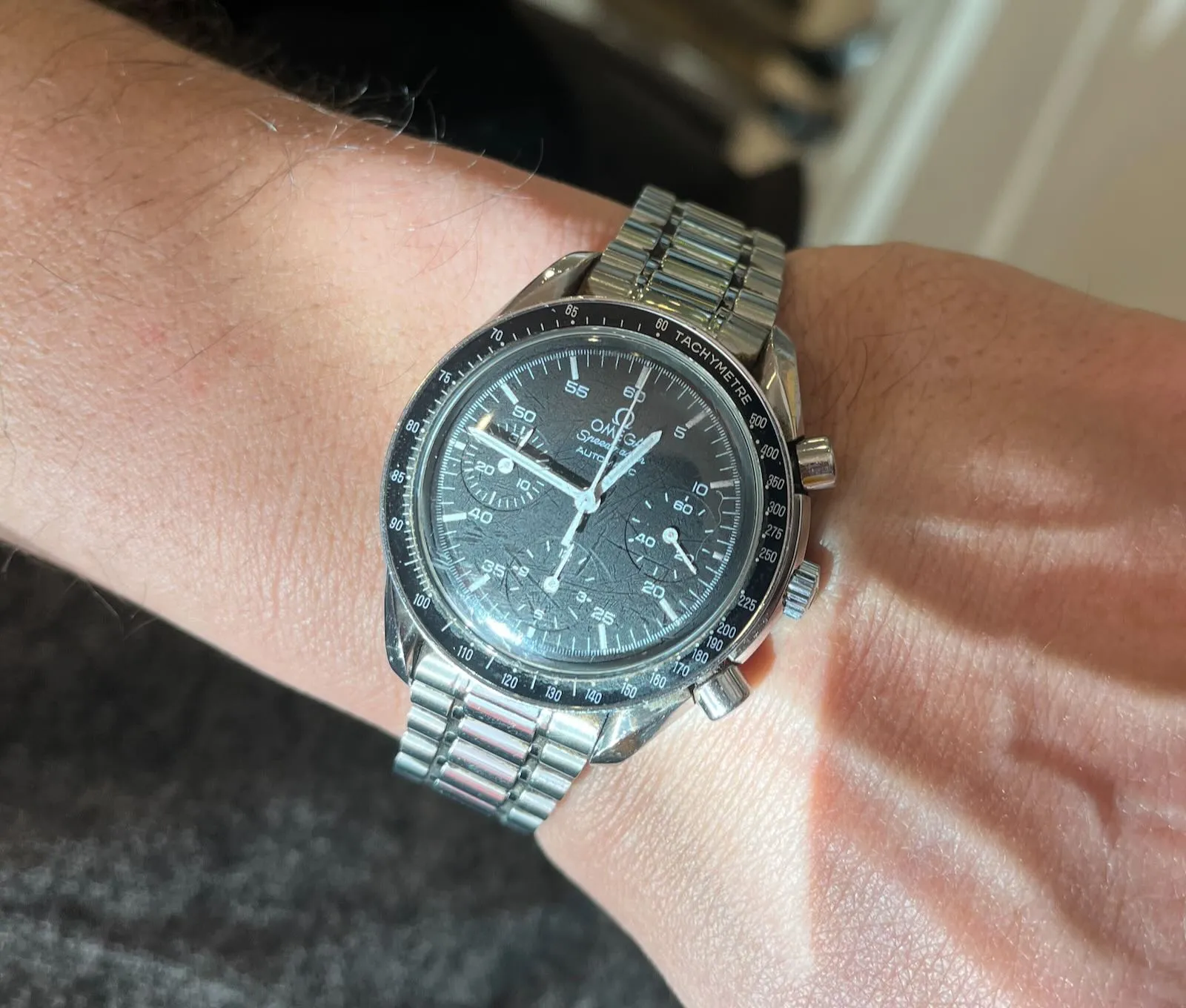 A large Omega wrist watch on someone’s wrist. There are quite a few dials, but the time is 14 minutes to one.