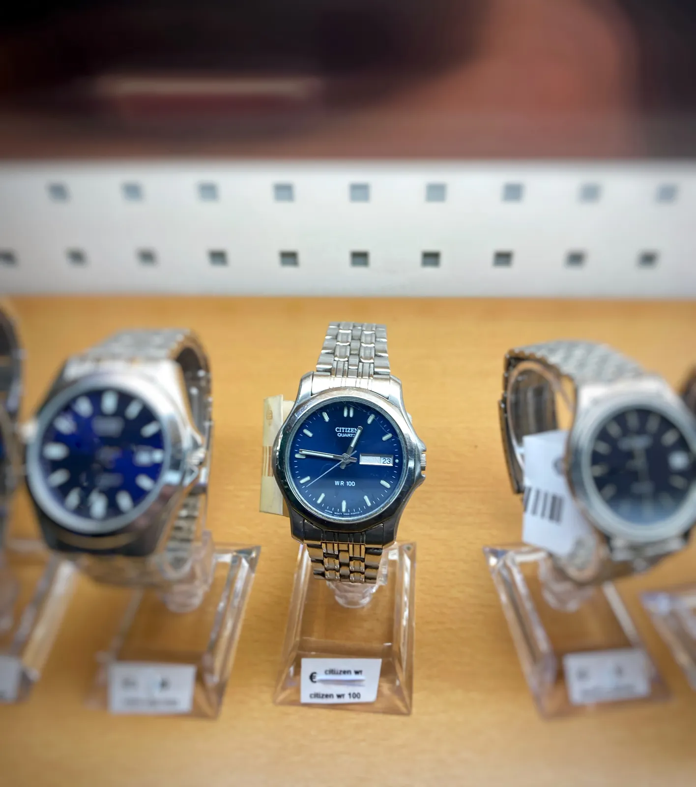 Three silver coloured metal wrist watches, all three with a dark blue face. The one in the middle is in focus. The time on this clock is 14 minutes to one.
