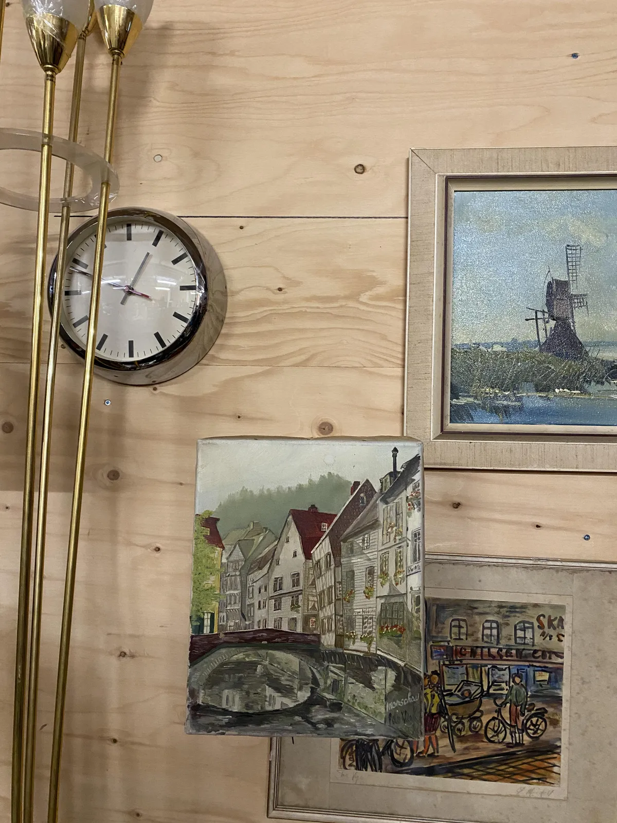 There are three paintings and a standing lamp on this picture. Behind the lamp there’s a clock that points at 12 to one.
