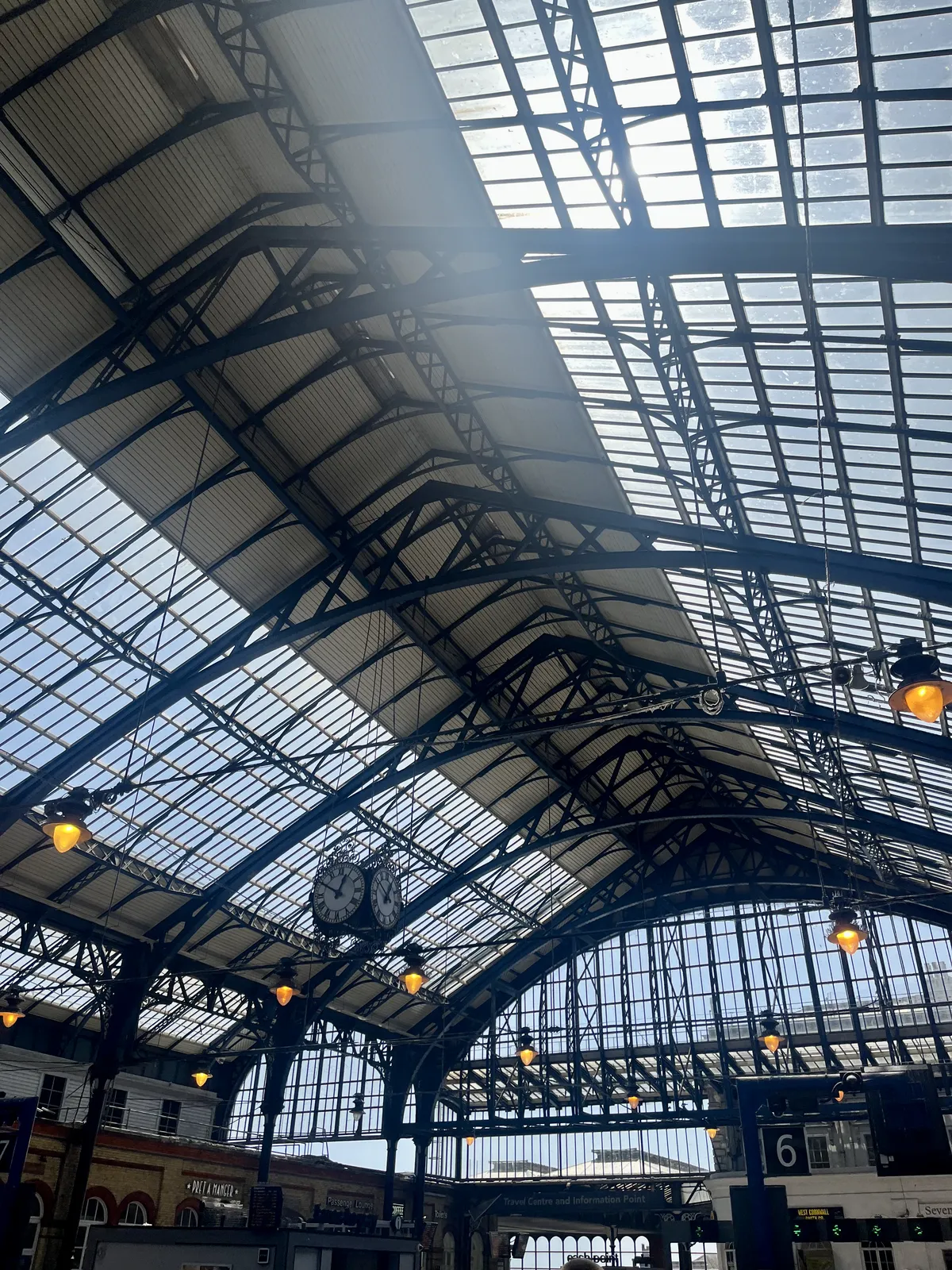 A huge, old cast iron station hall with a large clock hanging from its ceiling. It points at 10 to one.