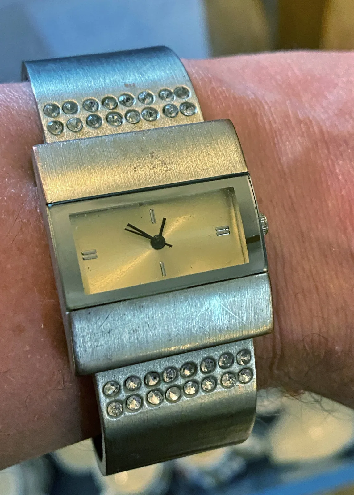 A very rectangular silver wristwatch (with a few diamonds). It seems to point at approximately 8 minutes to one.