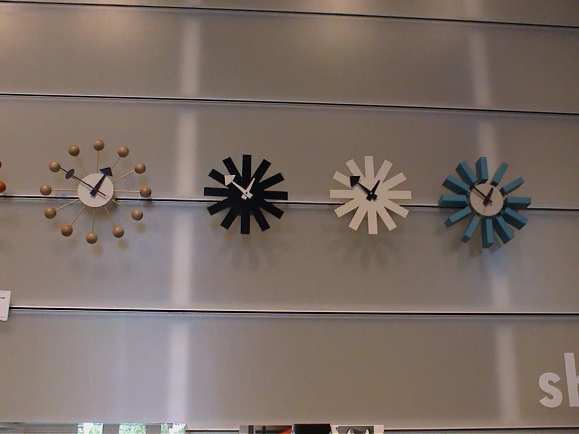 Four novelty clocks, high on a wall. one with coloured dots, the others with different types of rectangles. They all point at six to one.