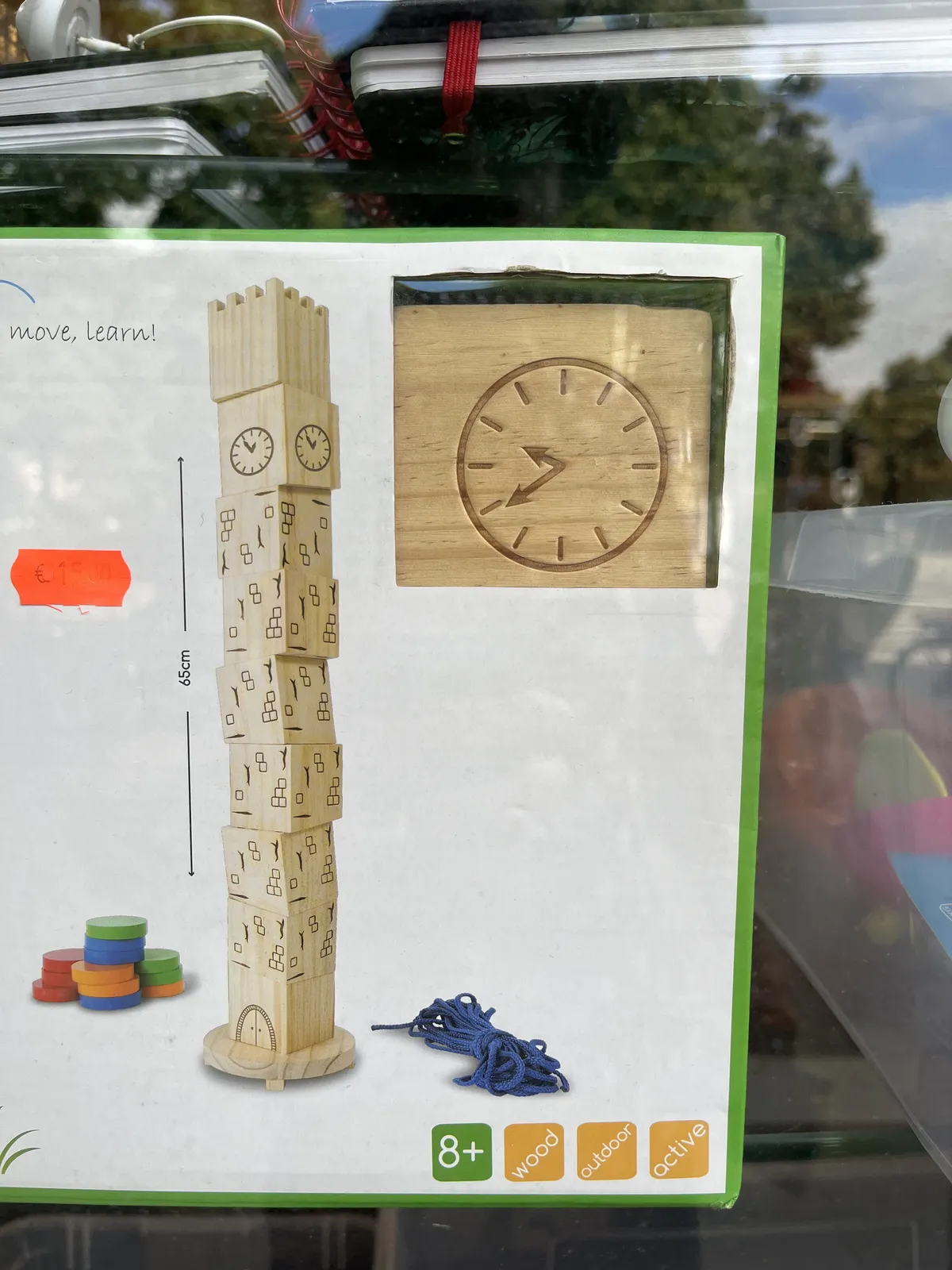 A picture of a box with wooden blocks in it. One of the blocks has a clock on it. On one picture on this box, the clocks are stacked. The upper block has the clock on it and it points at 6 minutes to one. On another picture the block with the clock is turned, and points at 39 minutes past nine.