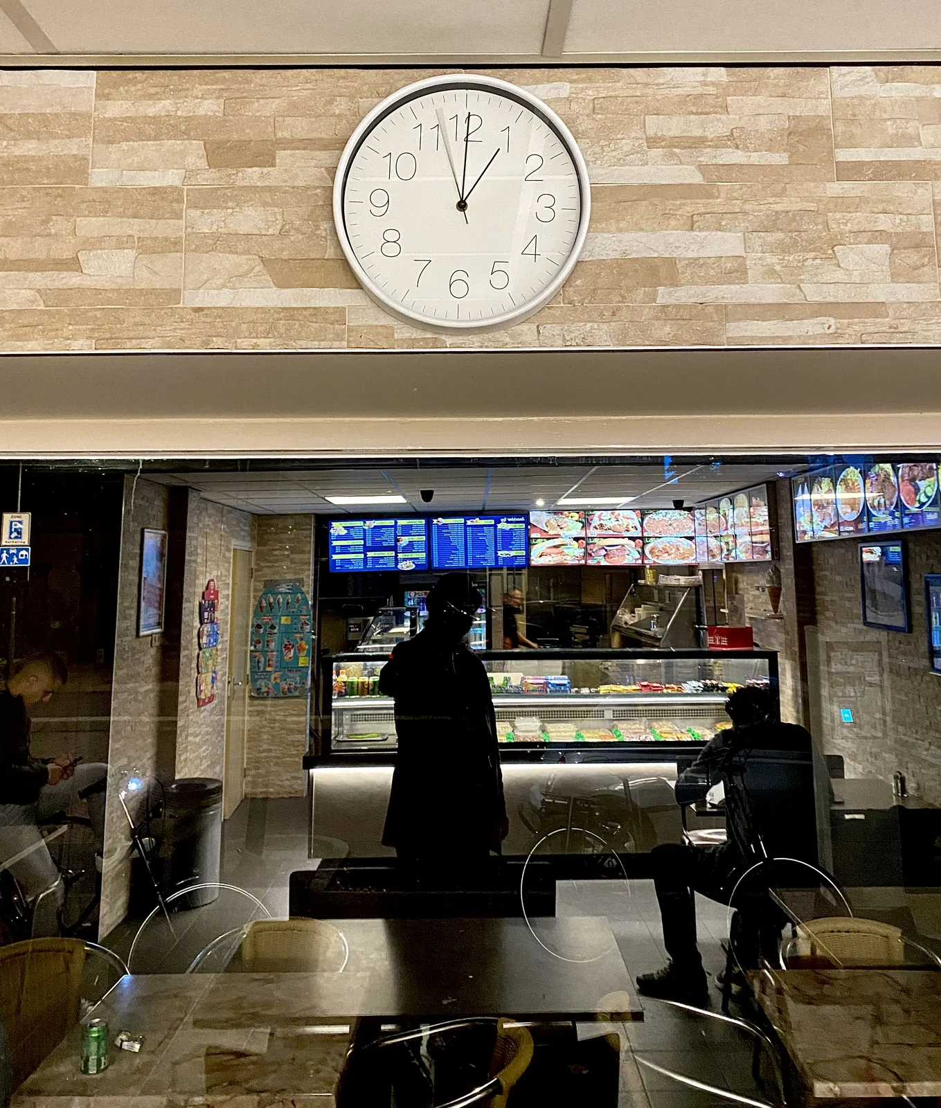 A picture taken in a snackbar. There’s a clock. The second hand is blurry because it’s moving. It’s one o’clock.