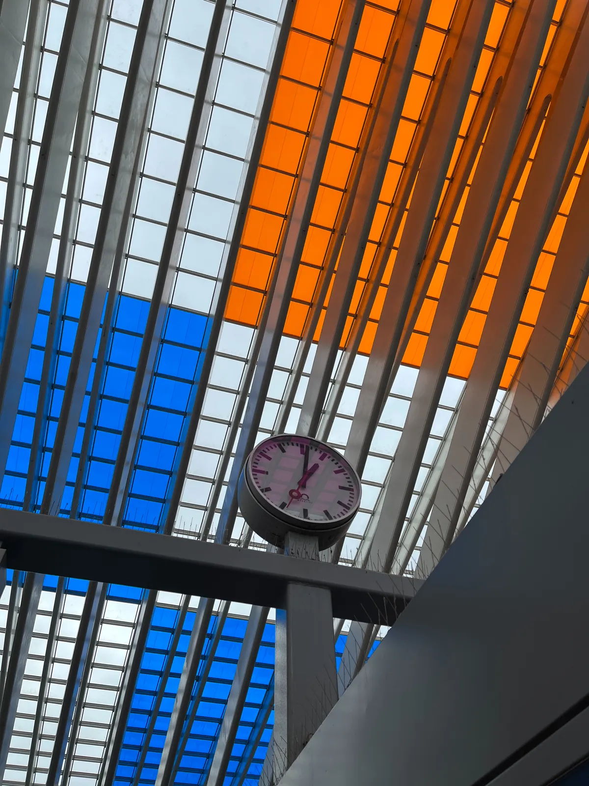 A colourful grid in the background. It consists of white, bright orange and bright blue squares. In the foreground there’s a clock that points at one minute past one.