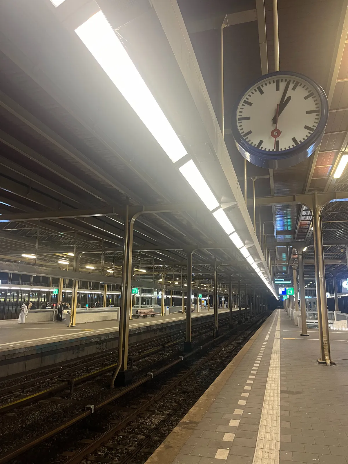 An older modernist clock on a seemingly deserted Dutch train station. It points at 3 minutes past 1.
