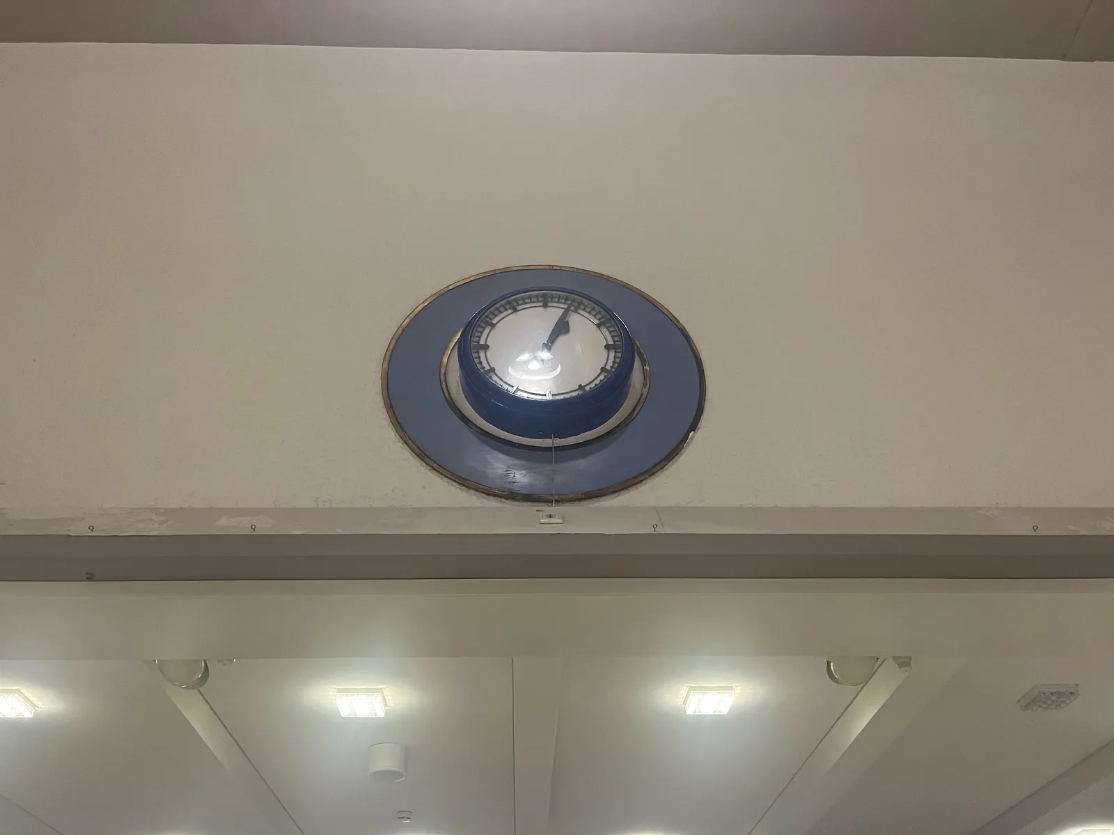 An old station clock. It points at 4 minutes past one. The lights reflecting in the protective glass look like a smiley.