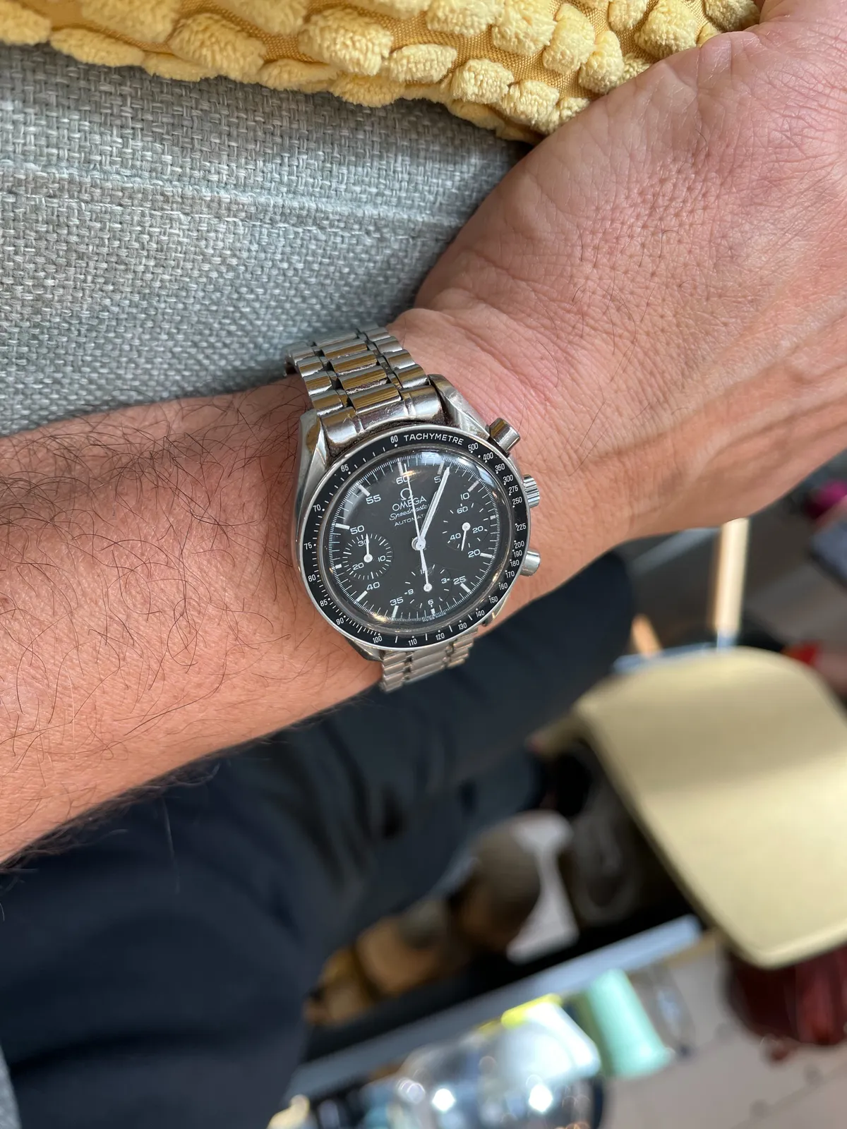 An Omega watch on someone’s wrist. It points at 6 minutes past one.
