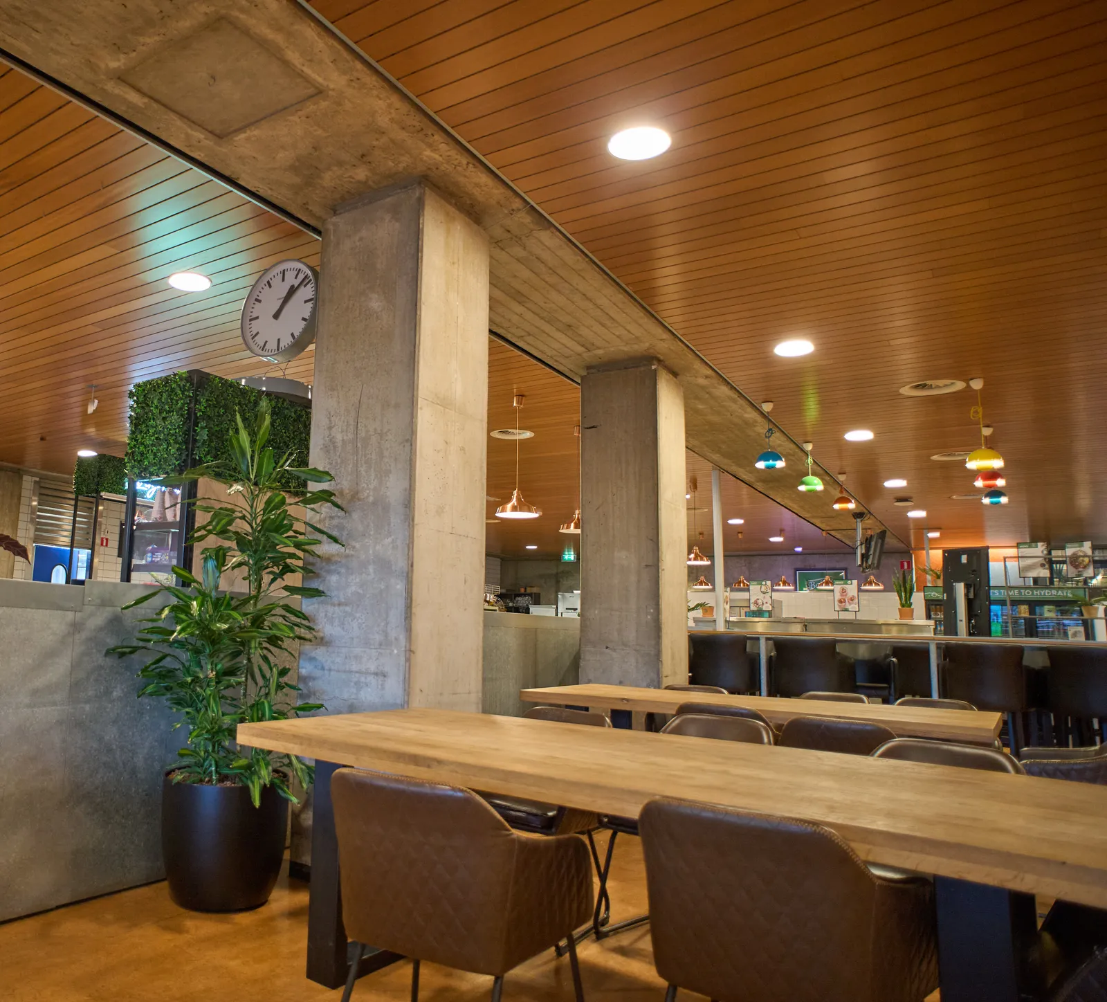 A wooden ceiling and lots of concrete in this university restaurant. There’s a clock attached to one of the monumental concrete pillars. It points at 8 minutes past one.