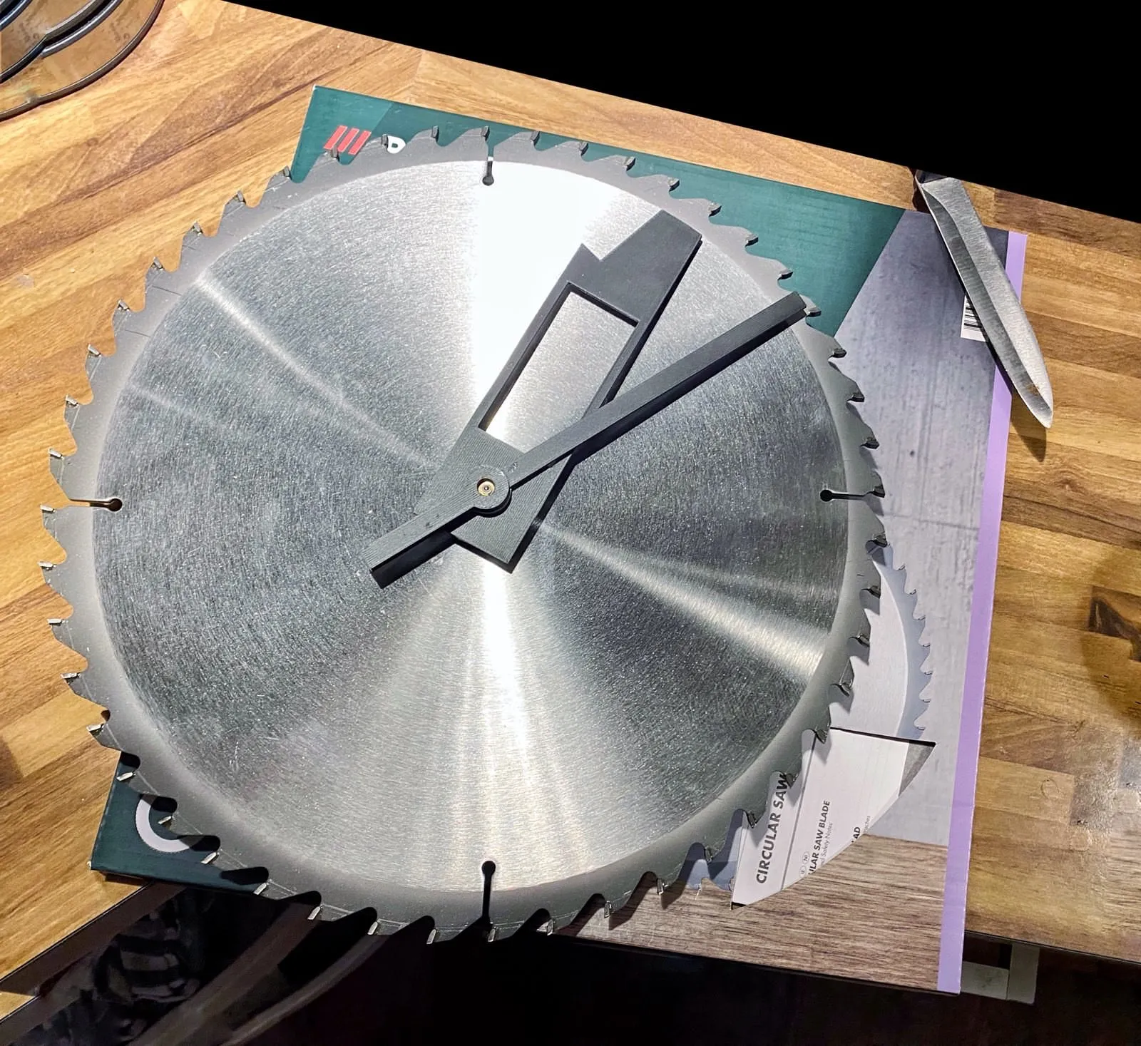 A clock made from a circular saw blade. It has 48 teeth, which makes it harder to read the time. It points at approximately 9 minutes past one.