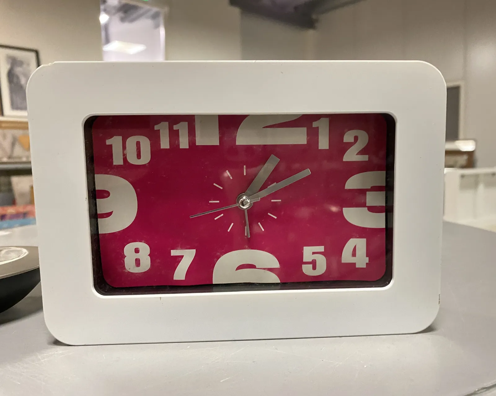 A rather expressive rectangular clock with large white type shouting the hours at us in white on red. It points at approximately 10 past one.