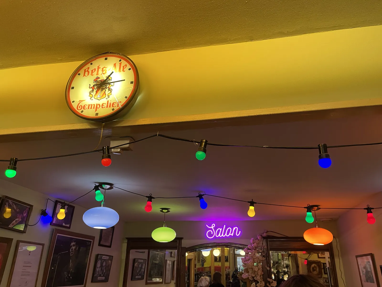 Colourful lamps, lots of picture frames on the walls, and a clock in this cafe. The clock points at 14 minutes past one.