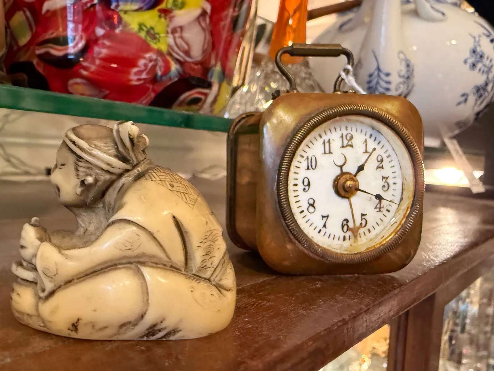 Next to a Japanese looking little statue of a sitting person, there’s a little old travel clock that points at 18 minutes past one.