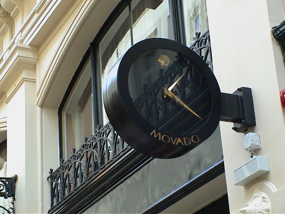 A black clock on a shop facade says it is 20 past one.
