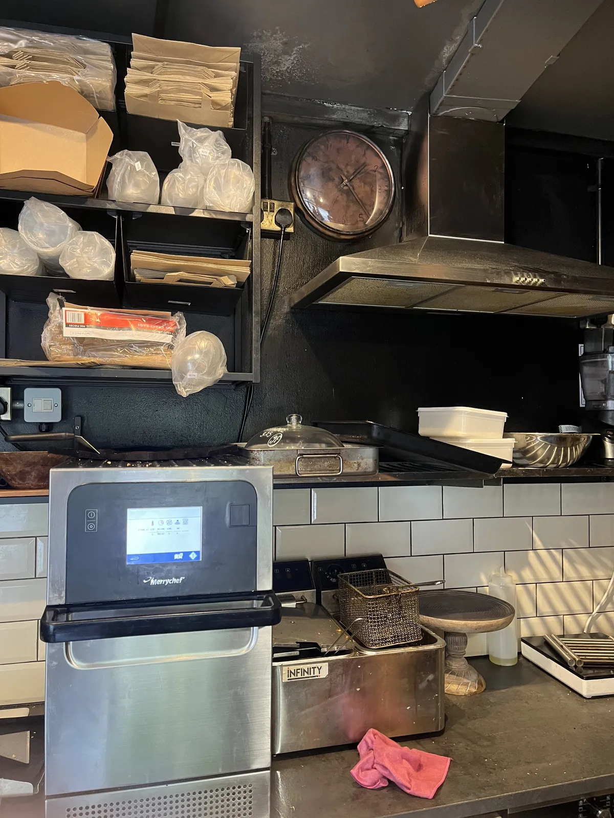 A picture taken in a dark kitchen. There’s a dark clock on the wall. It’s a bit hard to see what time it is, but once the eyes are accustomed to the darkness it is clear that it is 22 minutes past one.