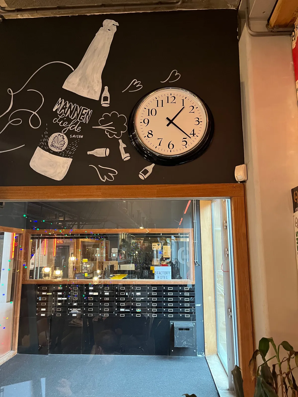 Looking through a large window into a hall way. Above the window a large beer bottle is drawn, next to a clock. The clock points at 22 minutes past one. 
