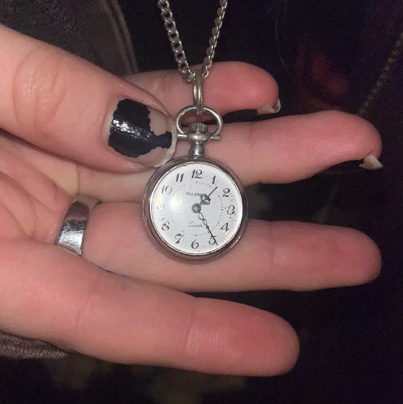 Someone is holding a small pocket watch, hanging from a chain, in their hand. The watch points at 24 minutes past one.