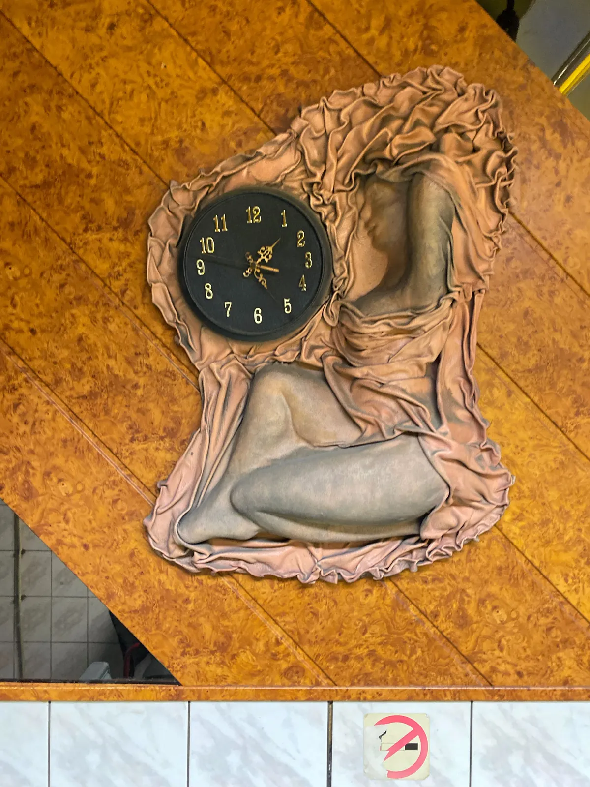 An art deco-style relief of a woman with a dress, or a sheet weirdly draped around her. In this sheet there’s a clock which points at 26 minutes past one.