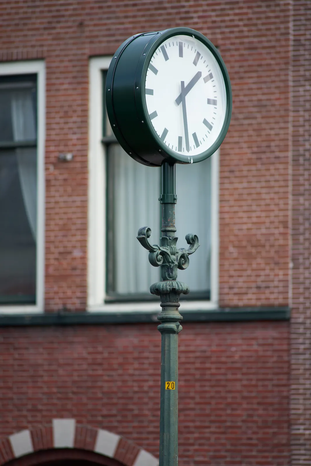 A clock attached to a pole that looks old. It points at 28 past one.