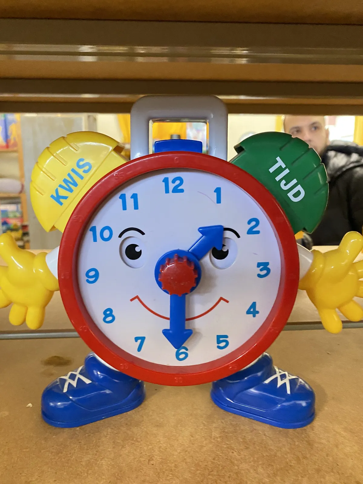 A very colourful toy clock, with a face and hands, points at half past one.